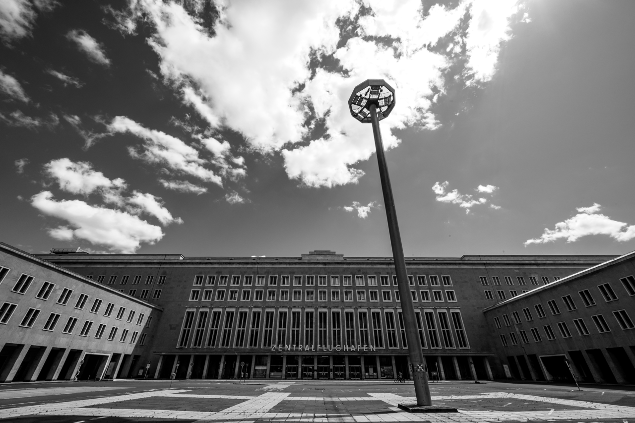 A black-and-white photo of the entrance to the old Tempelhof Terminal, with a utility pole in the foreground silhouetted against a cloud