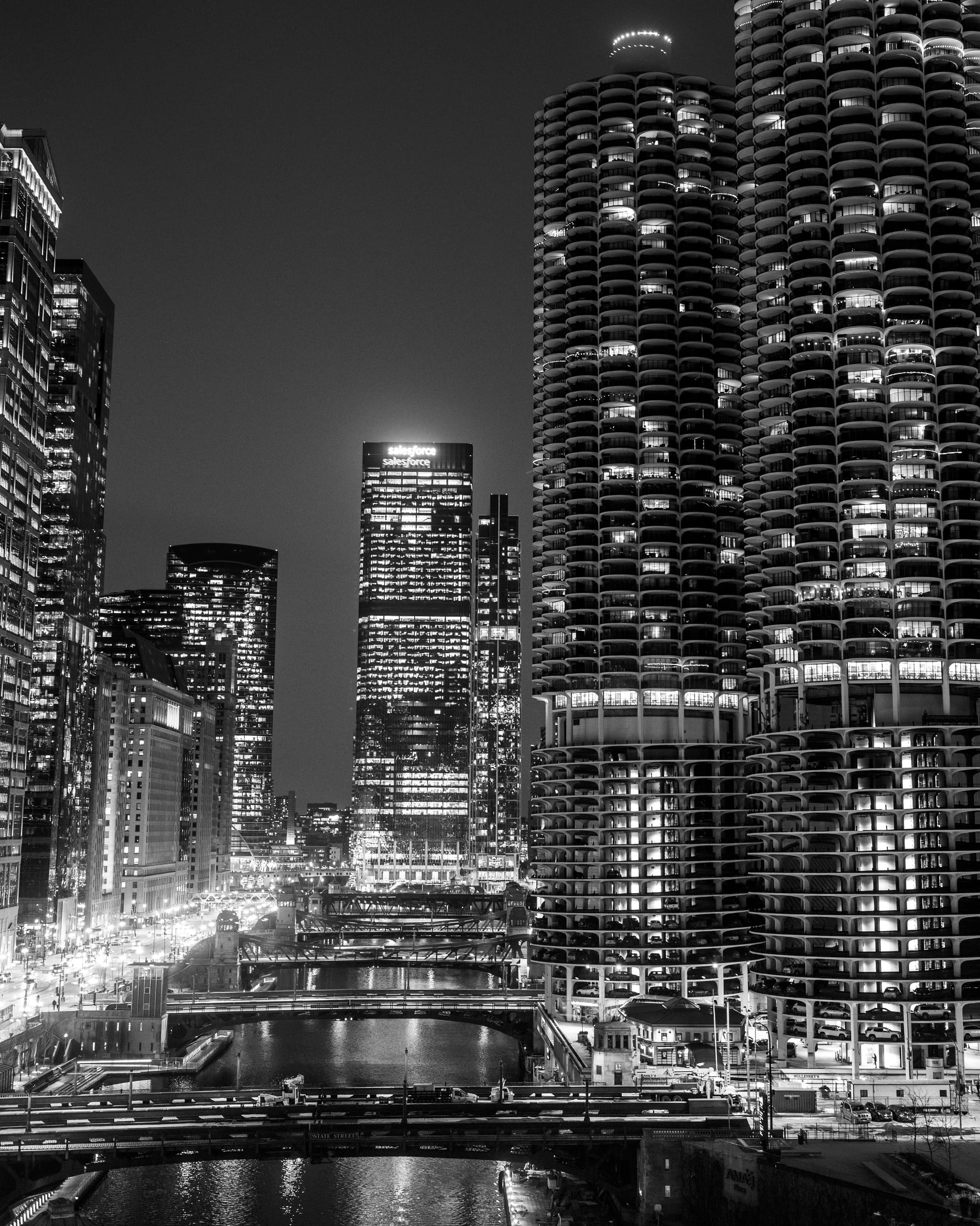 a black-and-white photograph of the Chicago River in the evening, with the buildings around it including the Marina City complex