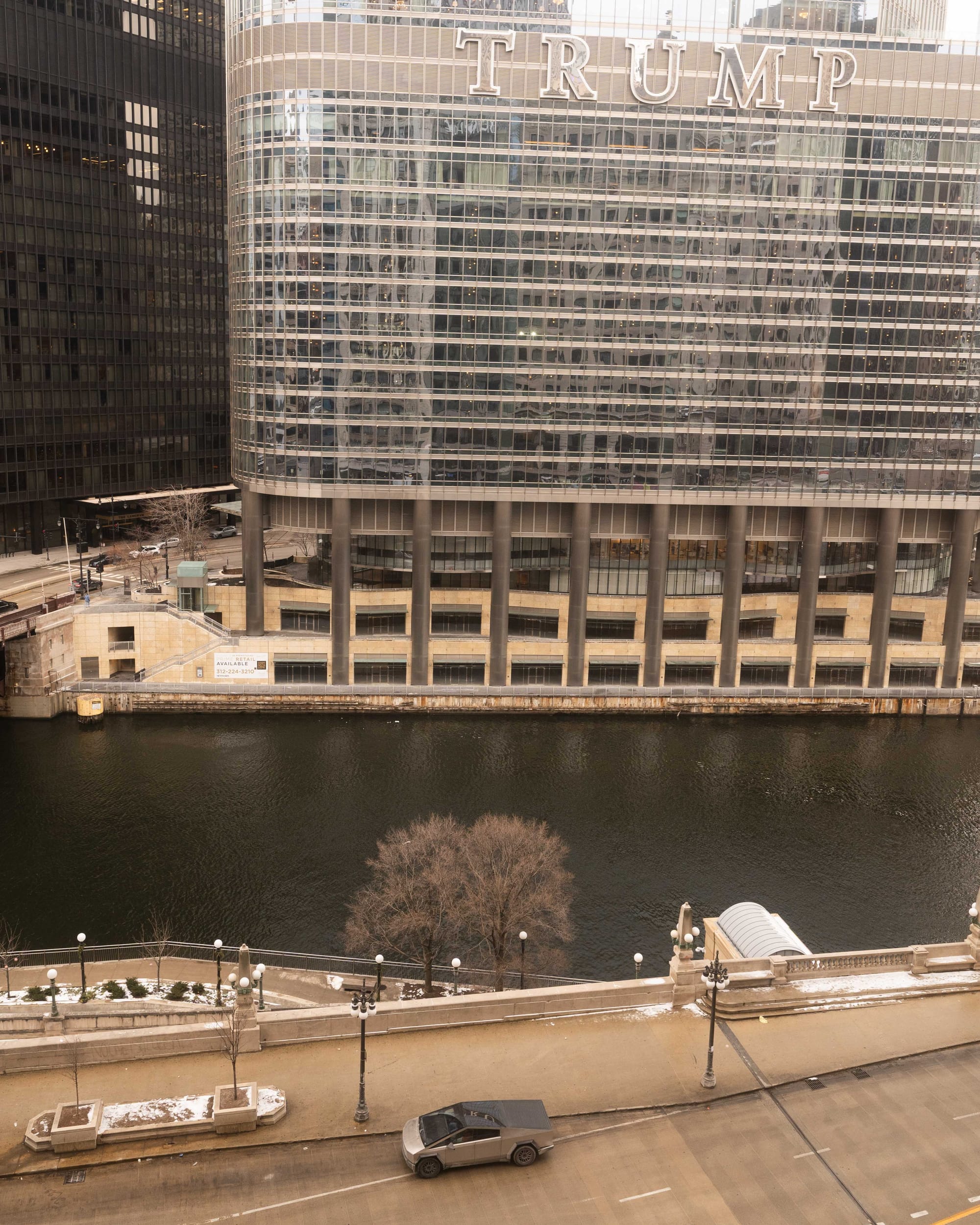 a photograph of Trump Tower in Chicago with a Cybertruck illegally parked across the river from it